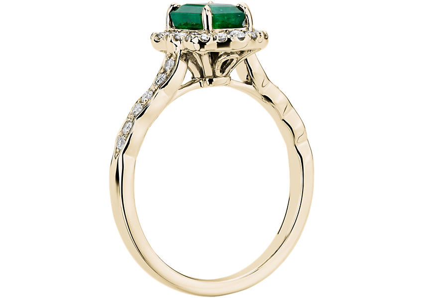 Vista lateral de un anillo de compromiso con esmeralda, halo de diamantes con motivo floral y engarce de oro amarillo.