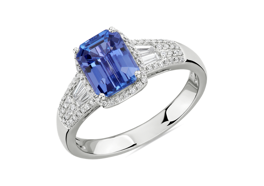 An emerald-cut tanzanite gemstone engagement ring surrounded by round diamond halo and accented by baguette and round diamonds through the white gold ring