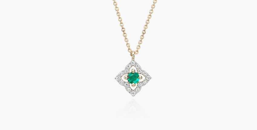 A floral, vintage-inspired May birthstone pendant with round emerald centre framed in diamond micropavé petals set in yellow gold and suspended from matching cable chain