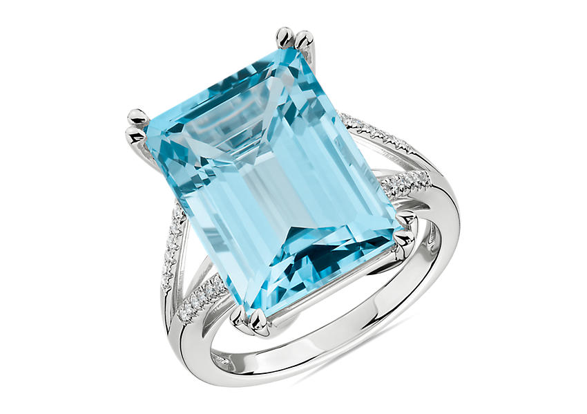 Un topacio azul de talla esmeralda de 16 por 12 milímetros en un anillo de compromiso con cuerpo dividido de oro blanco decorado con pavé de diamantes.