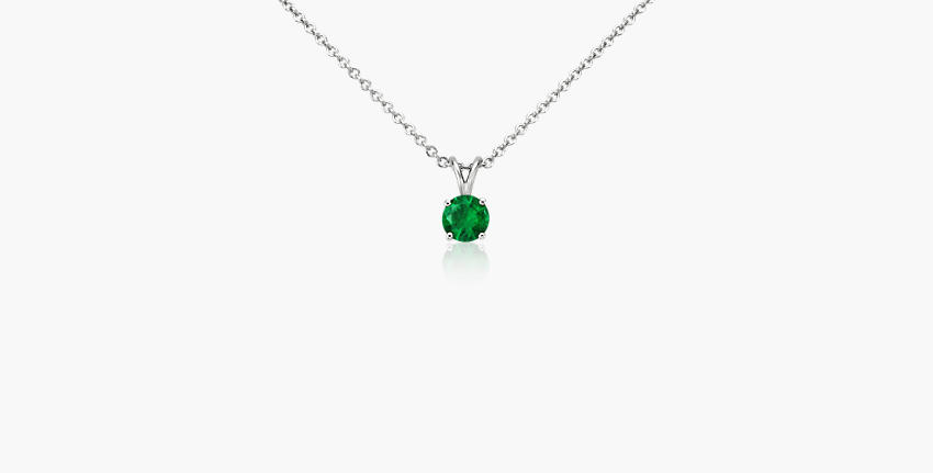 A round cut emerald gemstone featured in a solitaire pendant