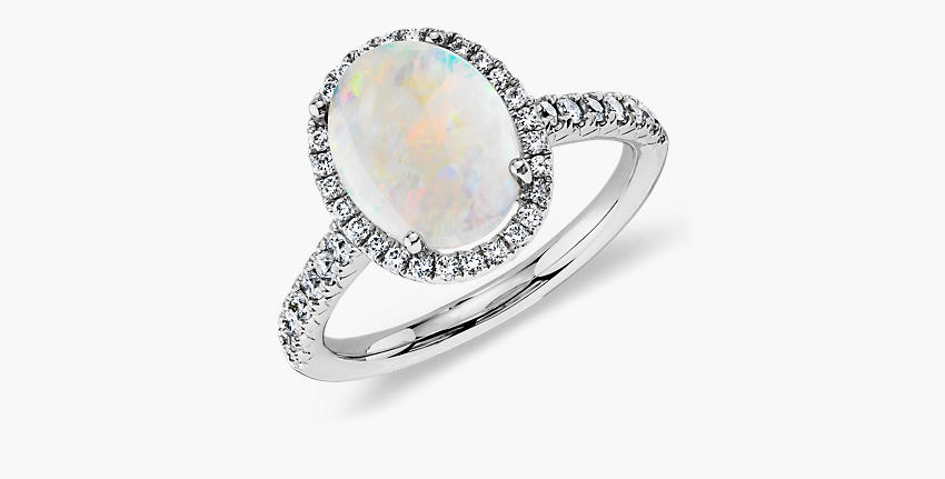 A white cabochon cut opal engagement ring with diamond pave halo set in white gold