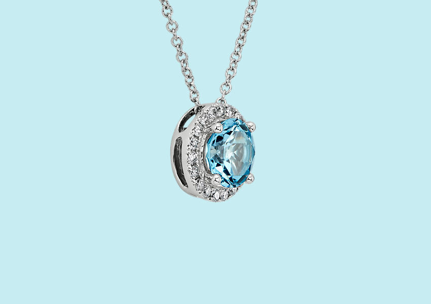 Un colgante con topacio azul de la  buena suerte con un halo de diamantes redondos en una cadena de oro blanco.