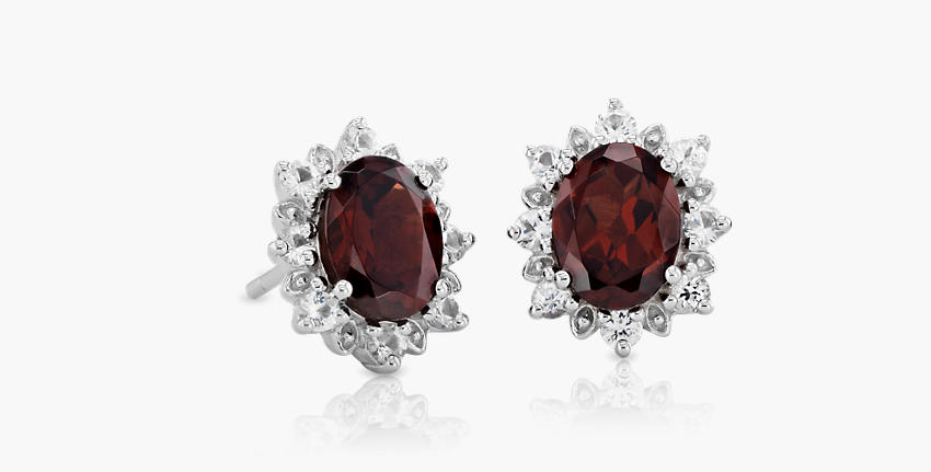 A pair of oval garnet gemstone earrings surrounded by symbolic sunburst diamond halo