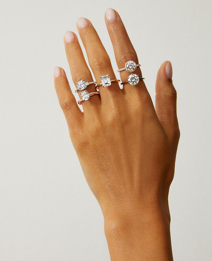 A woman's hand wearing five diamond engagement rings of different sizes