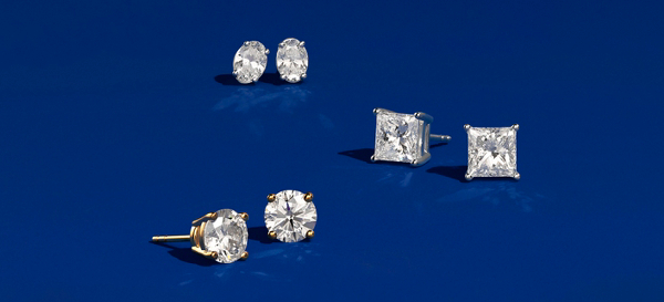 Four pairs of uniquely shaped diamond stud earrings set on a teal background.