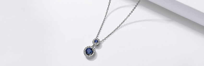 14k white gold pendant featuring two sapphires surrounded by diamond halos.