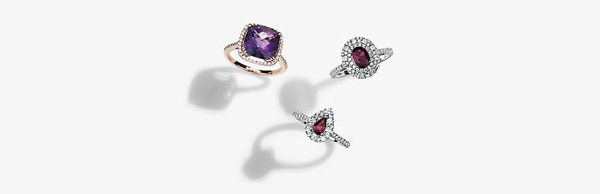 Two ruby gemstone rings set in diamond halos, and a rose gold ring set with an amethyst in a diamond halo.
