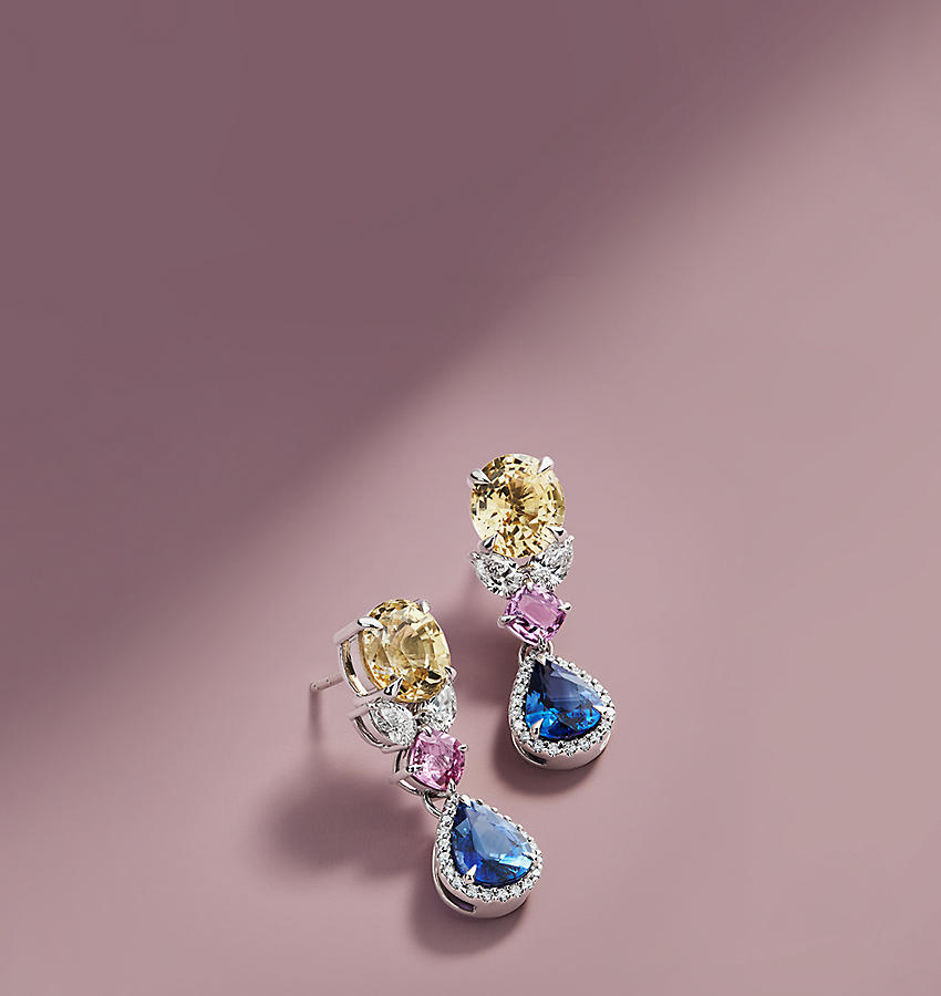 Des boucles d’oreilles ornées de gemmes jaunes, roses et bleues sur une surface rose