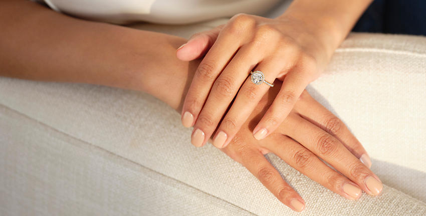 crossed white hands wearing beige nail polish and engagement ring resting on a sofa arm