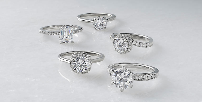 5 diamond engagement rings in various cuts and carats on shiny grey surface