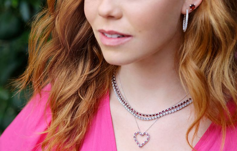 Woman with two eternity necklaces, a heart pendant, and diamond hoop earrings