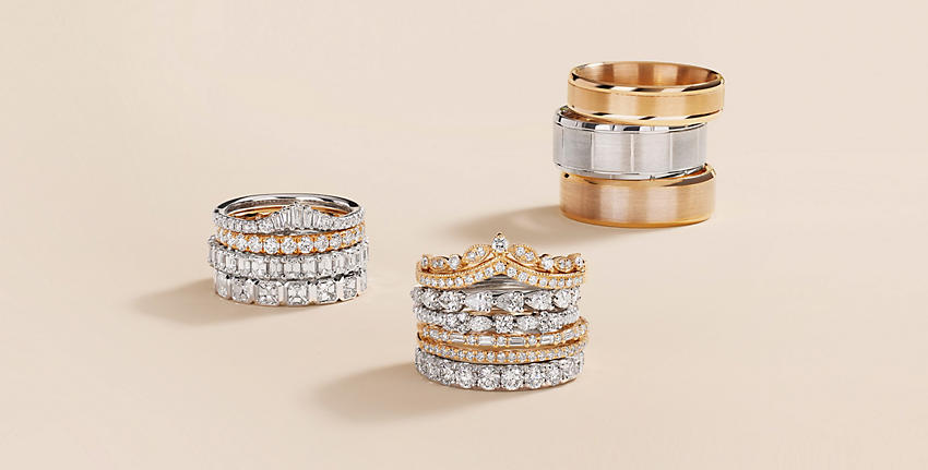 3 pilas de alianzas de bodas de metal y diamantes de varios quilates y metales, todo sobre una superficie beige