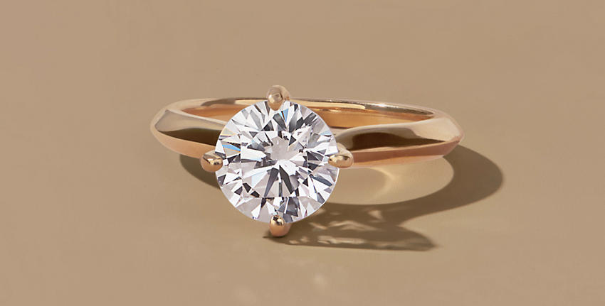 5 loose diamonds in varying cuts and 1 round engagement ring with gold band, all on beige background