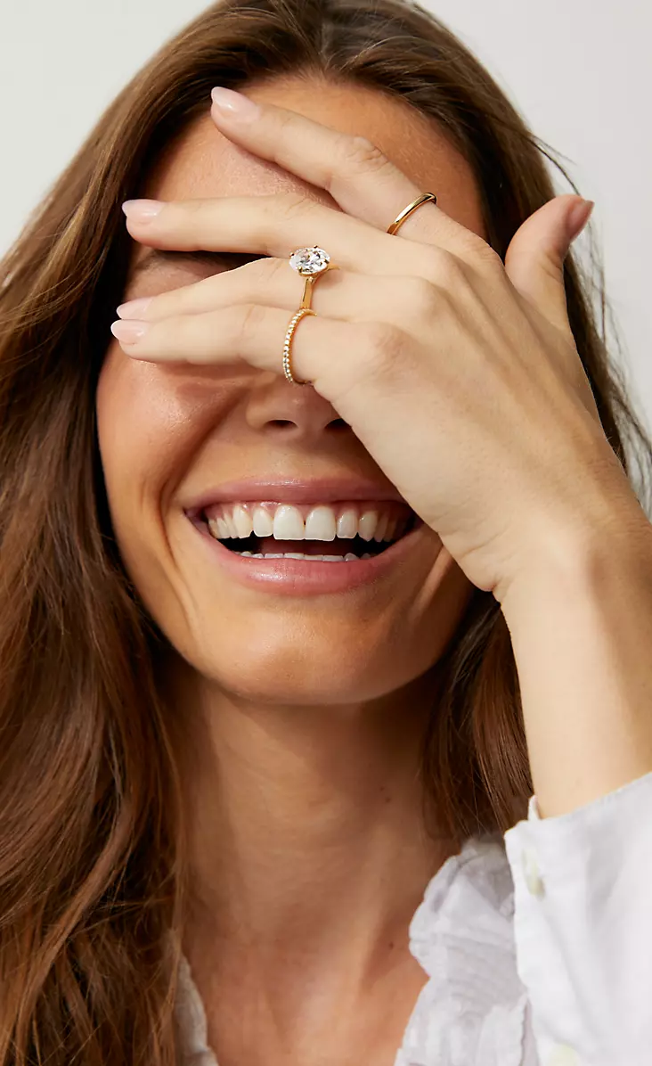 Mujer con la mano sobre los ojos, usando un anillo de compromiso con diamantes