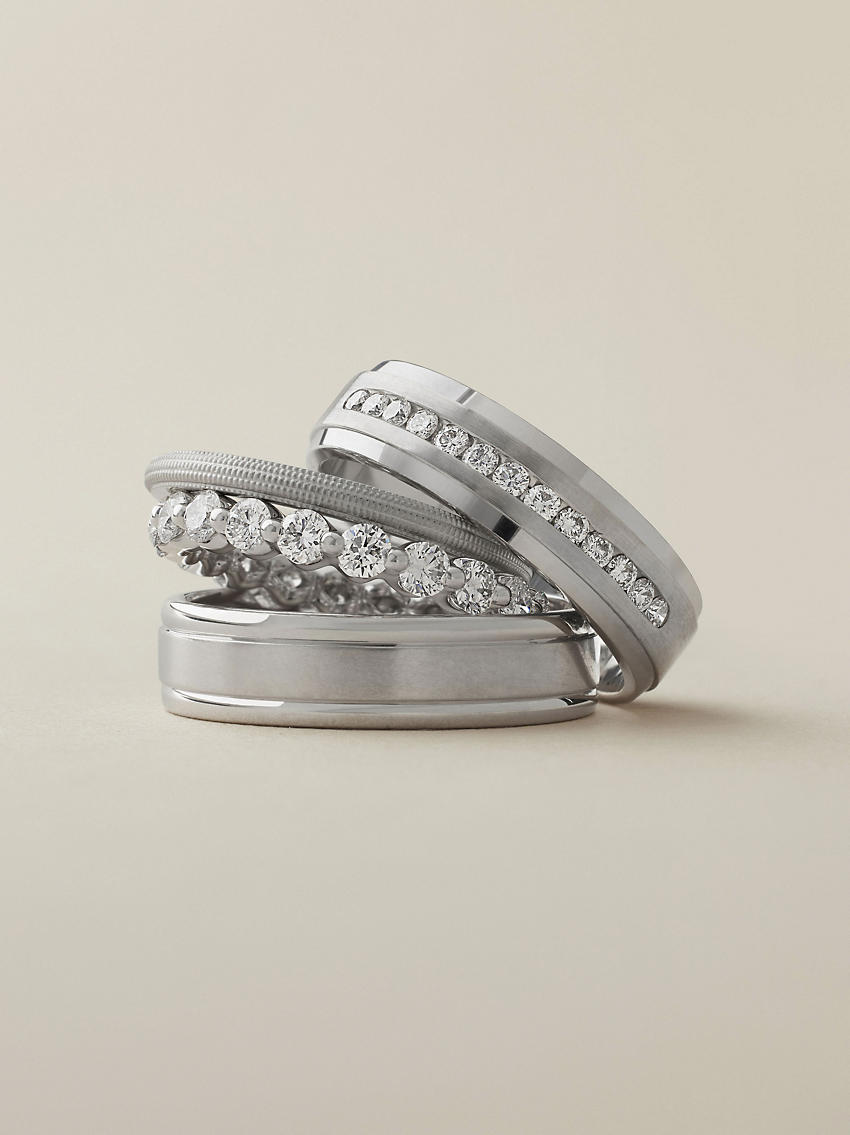 A channel set diamond platinum wedding ring stacked on top of two platinum wedding rings and a diamond eternity ring.