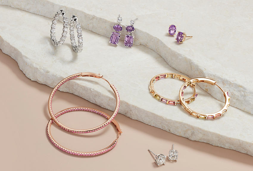 An assortment of jewelry featuring rose and yellow gold gemstone earrings, diamond eternity earrings, amethyst earrings and diamond studs.