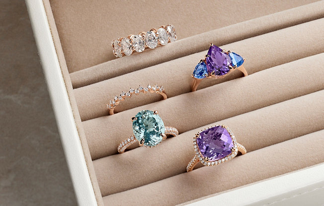 Five diamond and gemstone right hand rings in a ring holder.