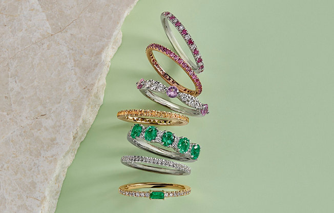 A stack of Blue Nile rings with emeralds, sapphire and gold.